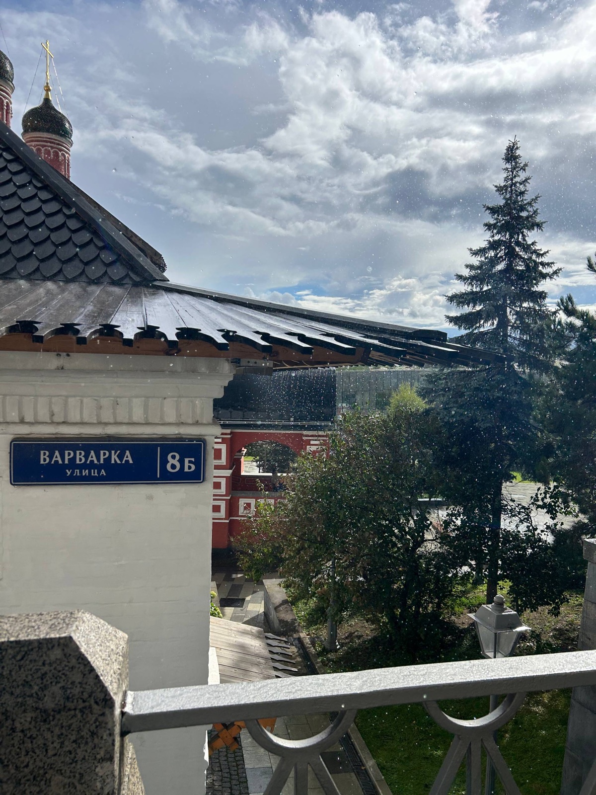 Табличка «Варварка, 8Б» на белой стене палат, за ней красные стены и купола — вид со смотровой площадки «Зарядья»